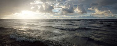 Gün batımında fırtınadan sonra Baltık Denizi kıyısında parlayan kümülüs bulutlarıyla açık bir gökyüzü. Dramatik bulut manzarası. Yumuşak altın güneş ışığı. Resimli bir manzara var. Kararsız hava, doğa, iklim değişikliği