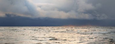 Gün batımında Baltık Denizi 'nin panoramik manzarası. Koyu renkli kümülüs bulutlarıyla dramatik bir gökyüzü. Su yüzeyi dokusu yakın çekim. Kararsız hava, kış, iklim değişikliği, doğa, çevre