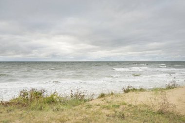 Fırtınadan sonra Baltık kıyısı (plaj). Kum tepeleri, kum tepeleri. Dramatik gökyüzü, dalgalar ve su sıçramaları. Doğa, ekoloji, kararsız hava, iklim değişikliği, eko-turizm, yürüyüş kavramları