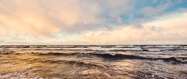 Gün batımında deniz kıyısında. Açık mavi gökyüzü, parlak pembe bulutlar, yumuşak ışık. Suyun simetri yansımaları, doğal ayna, su yüzeyi dokusu. Hava, iklim değişikliği, doğa. Idyllic deniz manzarası