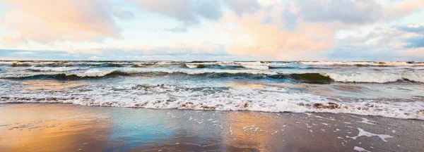 Gün batımında deniz kıyısında. Açık mavi gökyüzü, parlak pembe bulutlar, yumuşak ışık. Suyun simetri yansımaları, doğal ayna, su yüzeyi dokusu. Hava, iklim değişikliği, doğa. Idyllic deniz manzarası