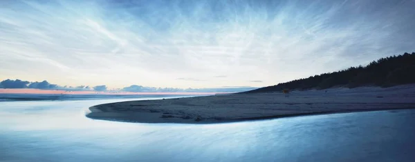 Starry sky with noctilucent clouds above the Baltic sea shore at summer solstice night. Golden flowing sunlight. Long exposure. Fantastic cloudscape. Natural pattern. Abstract art. Latvia