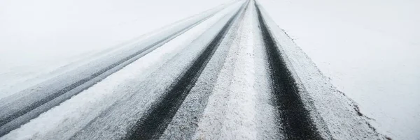 Snow-covered highway (asphalt road) through the country fields in a fog after a blizzard. Dangerous driving, climate change, global warming, ecology, environmental conservation