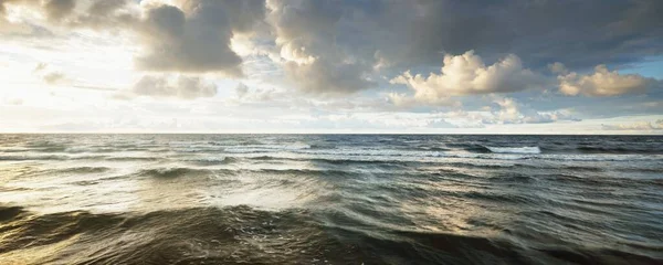Gün batımında fırtınadan sonra Baltık Denizi kıyısında parlayan kümülüs bulutlarıyla açık bir gökyüzü. Dramatik bulut manzarası. Yumuşak altın güneş ışığı. Resimli bir manzara var. Hava kararsız. Uzun pozlama