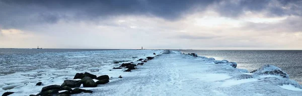 空の遊歩道と雪で覆われた防波堤が近くにあり バックグラウンドで凍ったバルト海 暗い嵐の雲 気候変動 地球温暖化の概念 長時間露光 — ストック写真