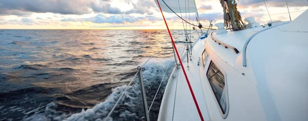 Gün batımında açık denizde yelken açmak. Güvertenin yakın görüntüsü, direk ve yelkenler. Yağmurdan sonra açık gökyüzü, çarpıcı parlayan bulutlar, altın güneş ışığı, dalgalar ve su sıçramaları, kasırga. Destansı deniz manzarası
