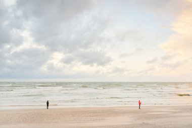 Baltic sea shore at sunset. Beach, sand dunes. Clear sunset sky, glowing clouds. Lonely people walking with a mobile phones. Local travel, eco tourism, mental health, social issues and distance themes