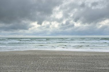 Baltık kıyıları (kum tepeleri) fırtınadan sonra gün batımında. Dramatik gökyüzü, parlayan bulutlar, rüzgar. Sonbahar manzarası. Doğa, çevre, ekoloji, kararsız hava, iklim değişikliği