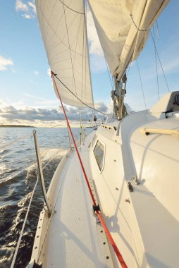 Gün batımında açık denizde yelken açmak. Güvertenin yakın görüntüsü, direk ve yelkenler. Yağmurdan sonra açık gökyüzü, çarpıcı parlayan bulutlar, altın güneş ışığı, dalgalar ve su sıçramaları, kasırga. Destansı deniz manzarası