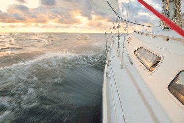 Gün batımında açık denizde yelken açmak. Güvertenin yakın görüntüsü, direk ve yelkenler. Yağmurdan sonra açık gökyüzü, çarpıcı parlayan bulutlar, altın güneş ışığı, dalgalar ve su sıçramaları, kasırga. Destansı deniz manzarası