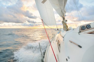 Gün batımında açık denizde yelken açmak. Güvertenin yakın görüntüsü, direk ve yelkenler. Yağmurdan sonra açık gökyüzü, çarpıcı parlayan bulutlar, altın güneş ışığı, dalgalar ve su sıçramaları, kasırga. Destansı deniz manzarası