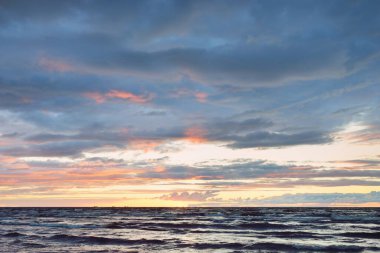 Gün batımında Baltık kıyılarından panoramik manzara. Dramatik fırtına gökyüzü, parlayan bulutlar, altın güneş ışığı. Dalgalar, su sıçratma. Doğa, çevre, kararsız hava