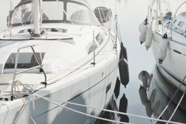 White modern sailboat (for rent and sale) moored to a pier in a yacht marina. Wooden teak deck. Nautical vessel, transportation, amateur sailing, vacations, cruising, recreation concepts
