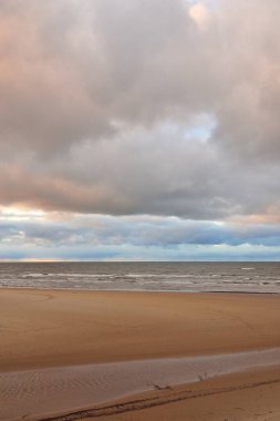 Gün batımında Baltık kıyısı. Kumsal manzarası (kum tepeleri). Dramatik günbatımı gökyüzü, parlayan bulutlar. Idyllic manzara. Doğa, tatiller, eğlence. Çevre turizmi. Panoramik görünüm