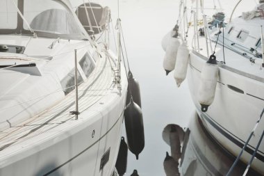 Beyaz modern yelkenli (kiralık ve satılık) yat limanındaki bir rıhtıma demirlemiş. Tahta meşe güvertesi. Denizcilik, ulaşım, amatör yelkencilik, tatiller, gezinti, eğlence kavramları