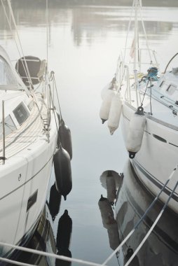 Beyaz modern yelkenli (kiralık ve satılık) yat limanındaki bir rıhtıma demirlemiş. Tahta meşe güvertesi. Denizcilik, ulaşım, amatör yelkencilik, tatiller, gezinti, eğlence kavramları