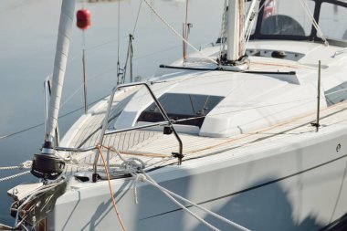 Beyaz modern yelkenli (kiralık ve satılık) yat limanındaki bir rıhtıma demirlemiş. Tahta meşe güvertesi. Denizcilik, ulaşım, amatör yelkencilik, tatiller, gezinti, eğlence kavramları