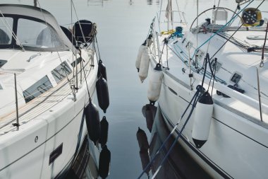 White modern sailboat (for rent and sale) moored to a pier in a yacht marina. Nautical vessel, transportation, amateur sailing, sport, leisure activity, vacations, cruising, recreation concepts