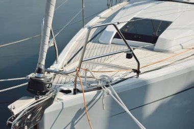 Beyaz modern yelkenli (kiralık ve satılık) yat limanındaki bir rıhtıma demirlemiş. Tahta meşe güvertesi. Denizcilik, ulaşım, amatör yelkencilik, tatiller, gezinti, eğlence kavramları