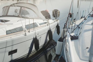 White modern sailboat (for rent and sale) moored to a pier in a yacht marina. Wooden teak deck. Nautical vessel, transportation, amateur sailing, vacations, cruising, recreation concepts