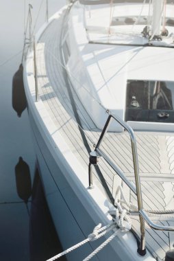 White modern sailboat (for rent and sale) moored to a pier in a yacht marina. Wooden teak deck. Nautical vessel, transportation, amateur sailing, vacations, cruising, recreation concepts