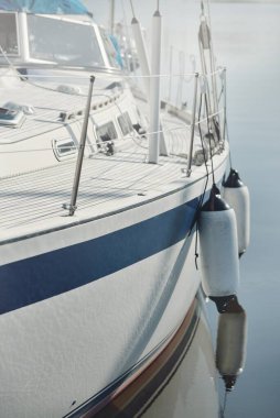 Beyaz modern yelkenli (kiralık ve satılık) yat limanındaki bir rıhtıma demirlemiş. Tahta meşe güvertesi. Denizcilik, ulaşım, amatör yelkencilik, tatiller, gezinti, eğlence kavramları
