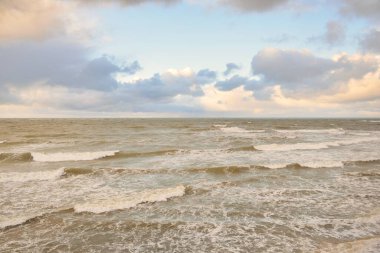 Gün batımında Baltık Denizi. Dramatik gökyüzü, mavi ve pembe parlayan bulutlar, altın güneş ışığı. Dalgalar, su sıçratma. Resimli manzara, deniz manzarası, doğa. Panoramik görünüm, uzun pozlama