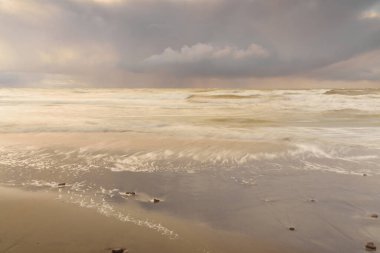 Gün batımında Baltık Denizi. Dramatik gökyüzü, mavi ve pembe parlayan bulutlar, altın güneş ışığı. Dalgalar, su sıçratma. Resimli manzara, deniz manzarası, doğa. Panoramik görünüm, uzun pozlama