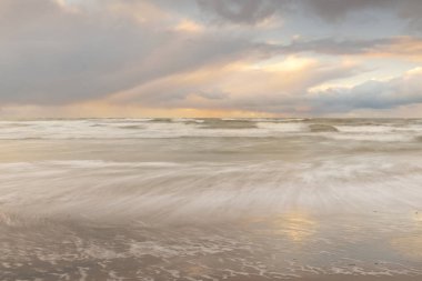 Gün batımında Baltık Denizi. Dramatik gökyüzü, mavi ve pembe parlayan bulutlar, altın güneş ışığı. Dalgalar, su sıçratma. Resimli manzara, deniz manzarası, doğa. Panoramik görünüm, uzun pozlama