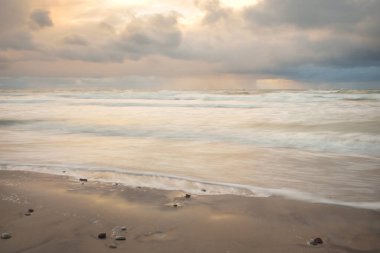 Gün batımında Baltık Denizi. Dramatik gökyüzü, mavi ve pembe parlayan bulutlar, altın güneş ışığı. Dalgalar, su sıçratma. Resimli manzara, deniz manzarası, doğa. Panoramik görünüm, uzun pozlama