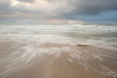 Gün batımında Baltık Denizi. Dramatik gökyüzü, mavi ve pembe parlayan bulutlar, altın güneş ışığı. Dalgalar, su sıçratma. Resimli manzara, deniz manzarası, doğa. Panoramik görünüm, uzun pozlama