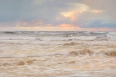 Baltic sea at sunset. Dramatic sky, blue and pink glowing clouds, golden sunlight. Waves, splashing water. Picturesque scenery, seascape, nature. Panoramic view, long exposure
