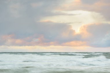 Gün batımında Baltık Denizi. Dramatik gökyüzü, mavi ve pembe parlayan bulutlar, altın güneş ışığı. Dalgalar, su sıçratma. Resimli manzara, deniz manzarası, doğa. Panoramik görünüm, uzun pozlama