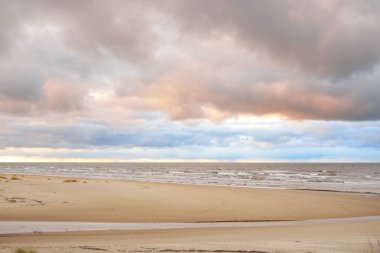 Gün batımında Baltık kıyısı. Kumsal manzarası (kum tepeleri). Dramatik günbatımı gökyüzü, parlayan bulutlar. Idyllic manzara. Doğa, tatiller, eğlence. Çevre turizmi. Panoramik görünüm