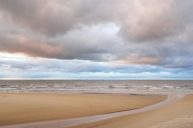 Gün batımında Baltık kıyısı. Kumsal manzarası (kum tepeleri). Dramatik günbatımı gökyüzü, parlayan bulutlar. Idyllic manzara. Doğa, tatiller, eğlence. Çevre turizmi. Panoramik görünüm