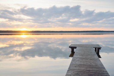 Forest lake (river) at sunset. Wooden pier. Glowing clouds, symmetry reflections in a still crystal clear water. Idyllic landscape. Nature, ecology, ecological reserve, ecotourism, hiking, vacations