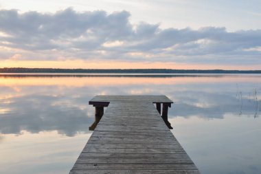 Orman Gölü (nehir) gün batımında. Ahşap iskele. Parlayan bulutlar, durgun ve berrak suda simetri yansımaları. Idyllic manzara. Doğa, ekoloji, ekolojik rezerv, eko-turizm, yürüyüş, tatiller
