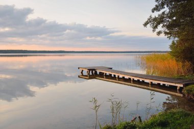 Orman Gölü (nehir) gün batımında. Ahşap iskele. Parlayan bulutlar, durgun ve berrak suda simetri yansımaları. Idyllic manzara. Doğa, ekoloji, ekolojik rezerv, eko-turizm, yürüyüş, tatiller