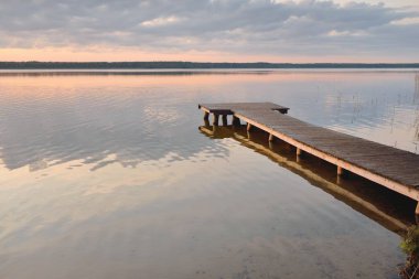 Orman Gölü (nehir) gün batımında. Ahşap iskele. Parlayan bulutlar, durgun ve berrak suda simetri yansımaları. Idyllic manzara. Doğa, ekoloji, ekolojik rezerv, eko-turizm, yürüyüş, tatiller