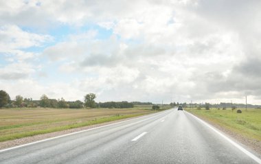 Tarlalar ve orman boyunca (asfalt yol) yol. Arabadan bak. Dramatik fırtına bulutları. Seyahat yerleri, rotalar, tatiller, lojistik, uzak yerler