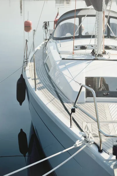 White modern sailboat (for rent and sale) moored to a pier in a yacht marina. Wooden teak deck. Nautical vessel, transportation, amateur sailing, vacations, cruising, recreation concepts