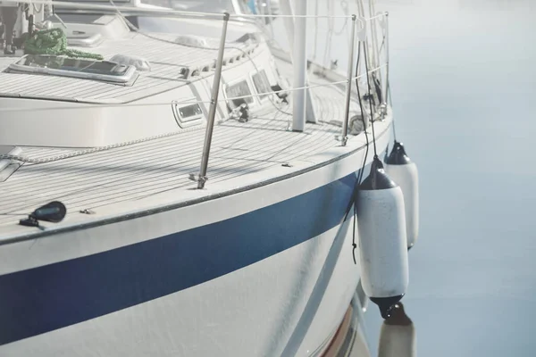 Beyaz modern yelkenli (kiralık ve satılık) yat limanındaki bir rıhtıma demirlemiş. Tahta meşe güvertesi. Denizcilik, ulaşım, amatör yelkencilik, tatiller, gezinti, eğlence kavramları