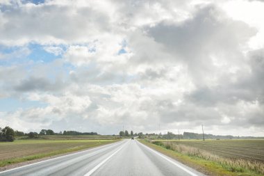 Tarlalar ve orman boyunca (asfalt yol) yol. Arabadan bak. Dramatik fırtına bulutları. Seyahat yerleri, rotalar, tatiller, lojistik, uzak yerler