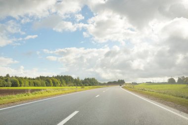 Tarlalar ve orman boyunca (asfalt yol) yol. Arabadan bak. Dramatik fırtına bulutları. Seyahat yerleri, rotalar, tatiller, lojistik, uzak yerler