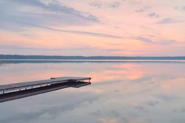 Gün batımında Orman Gölü. Ahşap iskele. Yumuşak güneş ışığı, parlayan bulutlar kristal berrak suda simetri yansımaları. Idyllic manzara. Panoramik manzara. Doğa, ekoloji, çevrecilik. Barış ve neşe kavramları