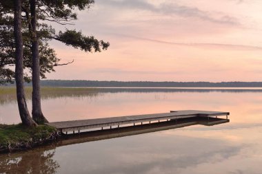 Gün batımında Orman Gölü. Ahşap iskele. Yumuşak güneş ışığı, parlayan bulutlar kristal berrak suda simetri yansımaları. Idyllic manzara. Panoramik manzara. Doğa, ekoloji, çevrecilik. Barış ve neşe kavramları
