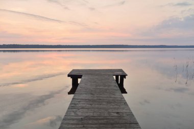 Forest lake at sunset. Wooden pier. Soft sunlight, glowing clouds, symmetry reflections in a crystal clear water. Idyllic landscape. Panoramic view. Nature, ecology, ecotourism, swimming, fishing