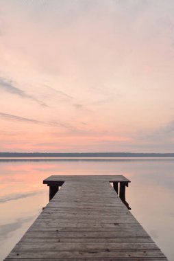 Forest lake at sunset. Wooden pier. Soft sunlight, glowing clouds, symmetry reflections in a crystal clear water. Idyllic landscape. Panoramic view. Nature, ecology, ecotourism. Peace and joy concepts