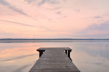 Forest lake at sunset. Wooden pier. Soft sunlight, glowing clouds, symmetry reflections in a crystal clear water. Idyllic landscape. Panoramic view. Nature, ecology, ecotourism. Peace and joy concepts