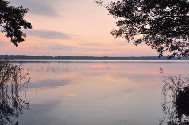 Gün batımında Orman Gölü. Yumuşak güneş ışığı, parlayan bulutlar kristal berrak suda simetri yansımaları. Idyllic manzara. Panoramik manzara. Doğa, ekoloji, çevrecilik. Barış ve neşe kavramları